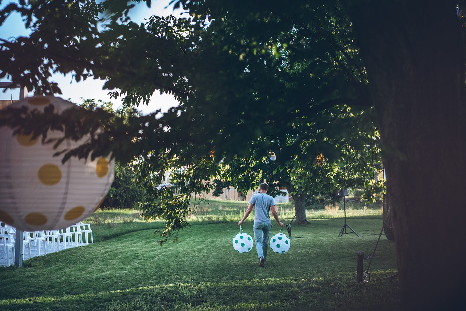 Caritas Stadtteilarbeit | Freiraum gestalten | © Amelie Chapalain Ein Teammitglied der Caritas Stadtteilarbeit bereitet einen Open Air Kino-Abend vor und trägt zwei Lampions über eine Wiese, um die Bäume damit zu dekorieren. | © Amelie Chapalain